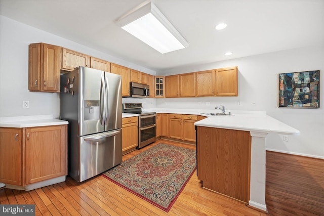 kitchen featuring kitchen peninsula, light hardwood / wood-style flooring, stainless steel appliances, a kitchen breakfast bar, and sink