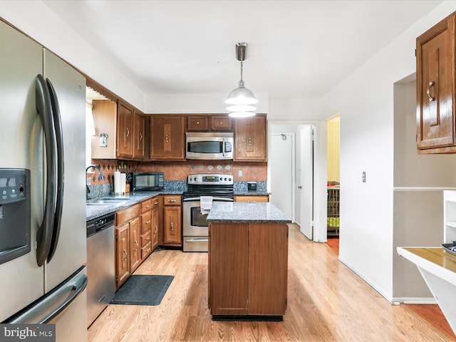 kitchen featuring sink, a center island, hanging light fixtures, stainless steel appliances, and light hardwood / wood-style flooring