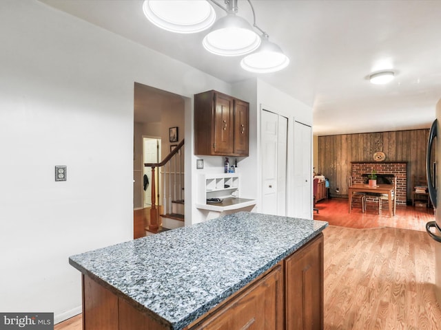 kitchen featuring wooden walls, light wood-type flooring, a fireplace, a kitchen island, and light stone counters