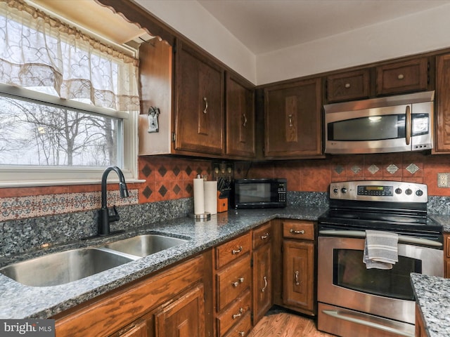 kitchen with decorative backsplash, appliances with stainless steel finishes, dark stone counters, sink, and light hardwood / wood-style flooring