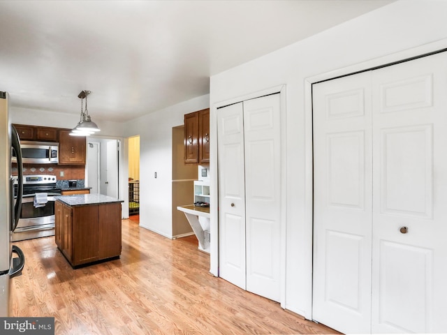 kitchen with stainless steel appliances, pendant lighting, light hardwood / wood-style floors, decorative backsplash, and a kitchen island