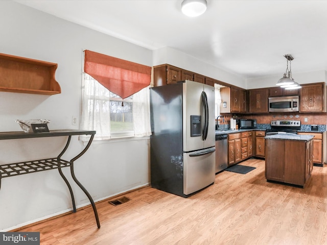 kitchen featuring appliances with stainless steel finishes, tasteful backsplash, decorative light fixtures, a center island, and light hardwood / wood-style floors