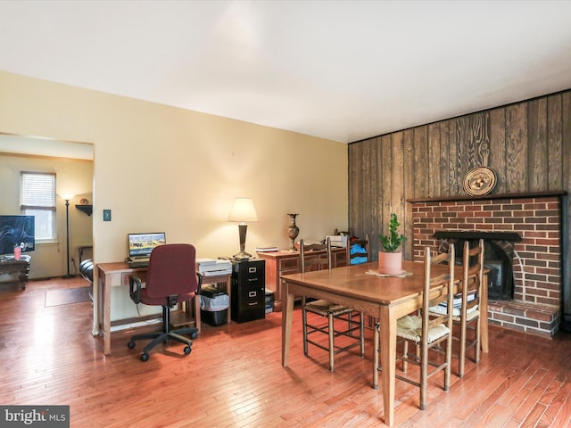 dining area with hardwood / wood-style flooring, wooden walls, and a brick fireplace