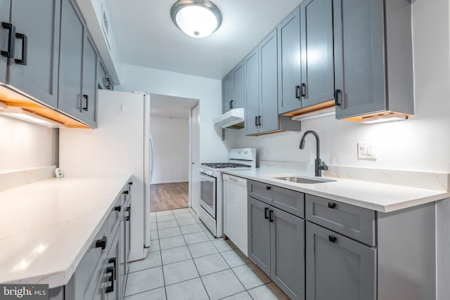 kitchen with light stone counters, sink, light tile patterned floors, and white appliances