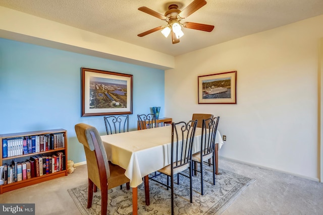 dining space with ceiling fan, light colored carpet, and a textured ceiling