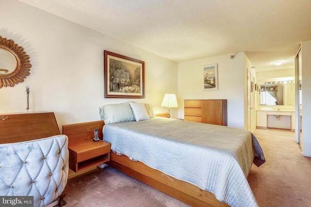 bedroom featuring ensuite bath, light colored carpet, and a textured ceiling