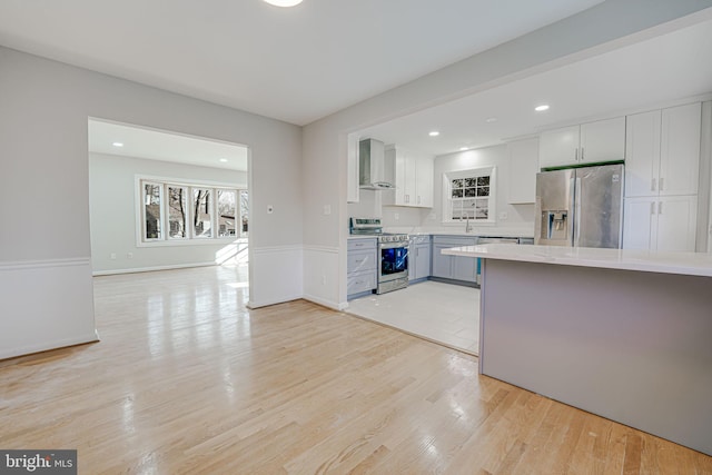 kitchen featuring stainless steel appliances, sink, wall chimney range hood, light hardwood / wood-style flooring, and white cabinets