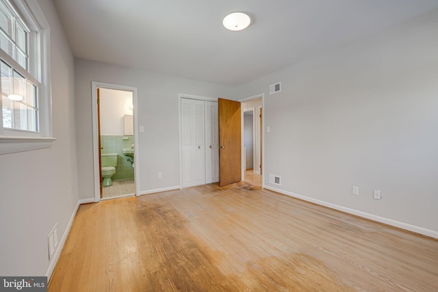 unfurnished bedroom featuring a closet, connected bathroom, and light hardwood / wood-style flooring