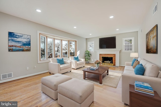 living room with a healthy amount of sunlight, light hardwood / wood-style floors, and a brick fireplace