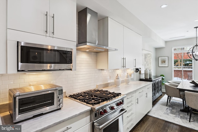 kitchen with appliances with stainless steel finishes, white cabinets, decorative light fixtures, and wall chimney range hood