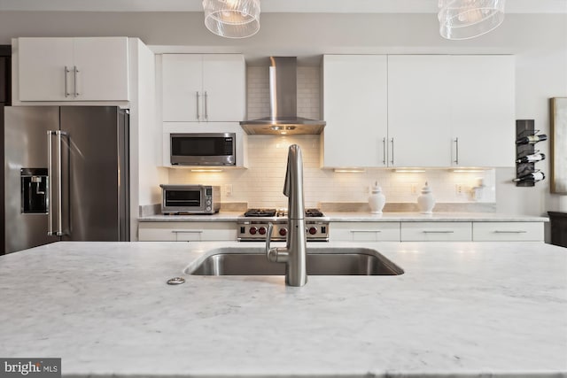 kitchen with light stone counters, pendant lighting, wall chimney exhaust hood, and stainless steel appliances