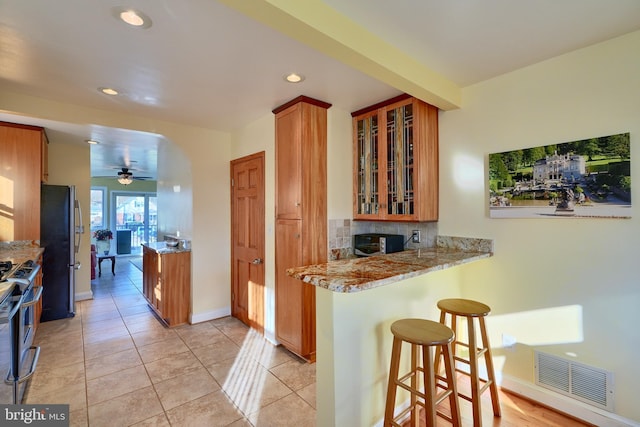 kitchen featuring kitchen peninsula, a kitchen bar, tasteful backsplash, stainless steel appliances, and ceiling fan