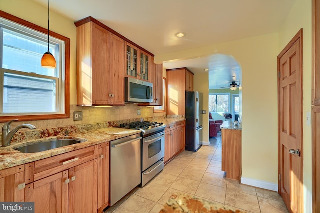 kitchen featuring sink, ceiling fan, light stone countertops, appliances with stainless steel finishes, and decorative light fixtures