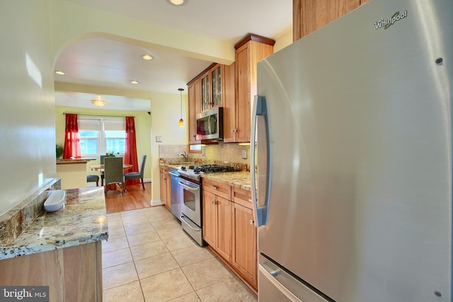 kitchen featuring light stone countertops, light tile patterned floors, tasteful backsplash, decorative light fixtures, and stainless steel appliances