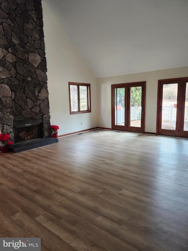 unfurnished living room featuring a stone fireplace, wood-type flooring, and high vaulted ceiling