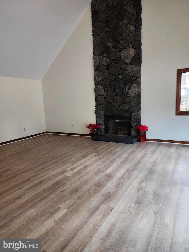 unfurnished living room featuring light hardwood / wood-style floors, a stone fireplace, and lofted ceiling