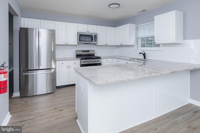 kitchen with white cabinetry, kitchen peninsula, stainless steel appliances, and light hardwood / wood-style flooring