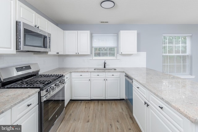 kitchen with light stone countertops, light wood-type flooring, stainless steel appliances, sink, and white cabinetry