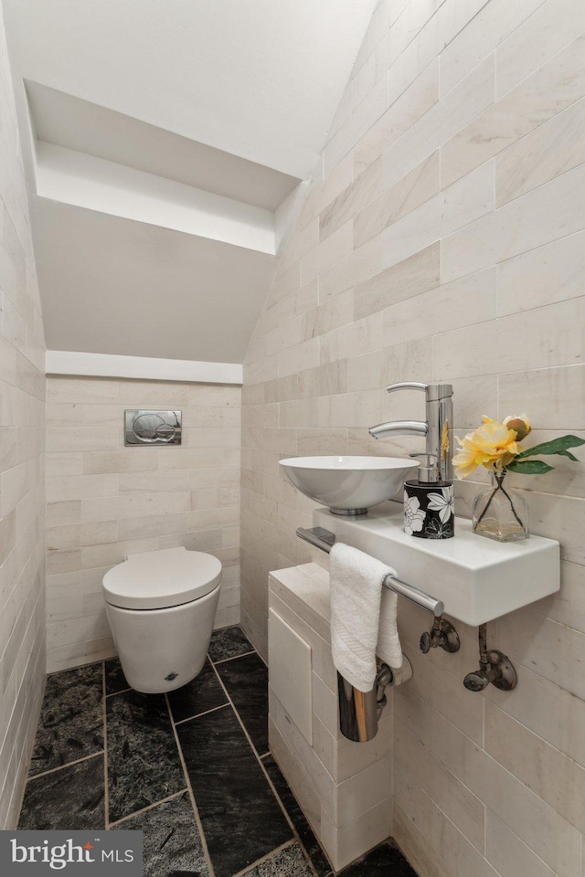 bathroom featuring vaulted ceiling, toilet, tile walls, and a sink