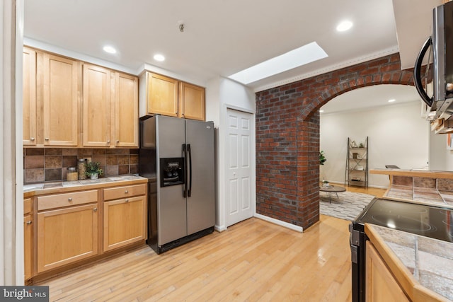 kitchen with black electric range oven, arched walkways, brick wall, stainless steel fridge with ice dispenser, and light wood finished floors