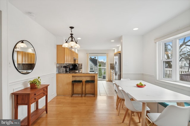 kitchen with kitchen peninsula, decorative backsplash, light brown cabinetry, decorative light fixtures, and light hardwood / wood-style floors