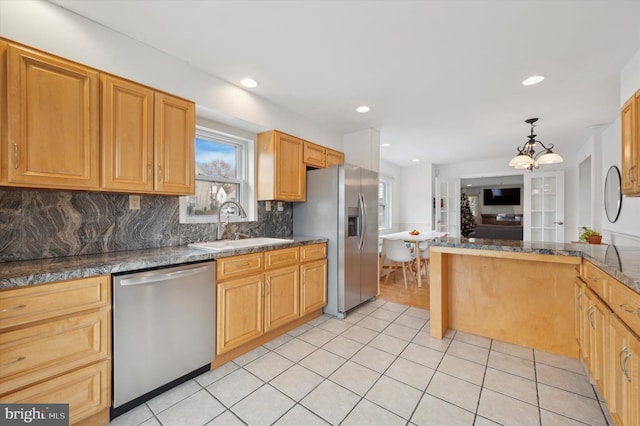 kitchen with sink, hanging light fixtures, stainless steel appliances, backsplash, and dark stone counters