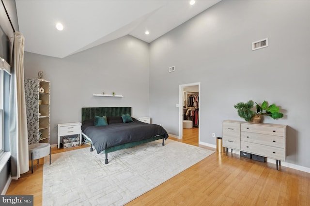 bedroom with hardwood / wood-style floors, a walk in closet, high vaulted ceiling, and a closet