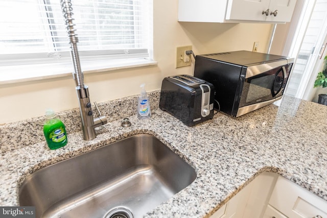 room details with white cabinetry, sink, and light stone countertops