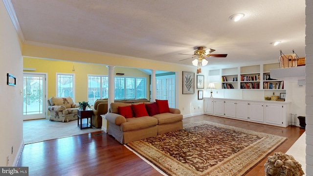 living room with wood-type flooring, ornate columns, ceiling fan, and crown molding