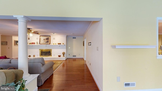 living room featuring ceiling fan, ornamental molding, a large fireplace, wood-type flooring, and decorative columns