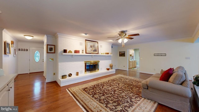 living room with ceiling fan, light hardwood / wood-style flooring, ornamental molding, and a brick fireplace