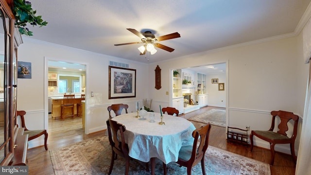 dining area featuring built in shelves, light wood-type flooring, ceiling fan, and crown molding