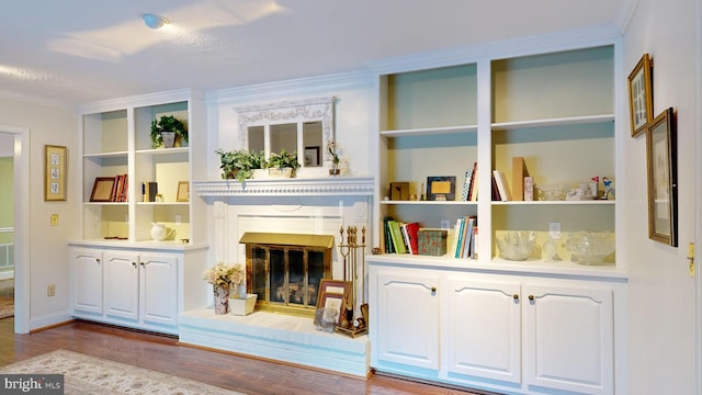 living area featuring built in shelves, crown molding, wood-type flooring, and a brick fireplace