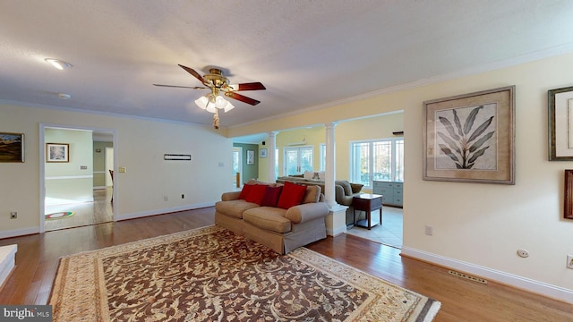 living room featuring ornate columns, ceiling fan, light wood-type flooring, a textured ceiling, and ornamental molding