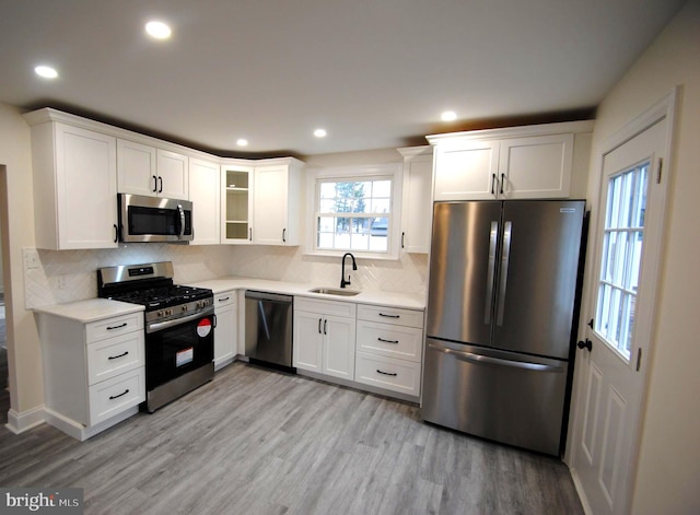 kitchen with sink, stainless steel appliances, light hardwood / wood-style floors, decorative backsplash, and white cabinets