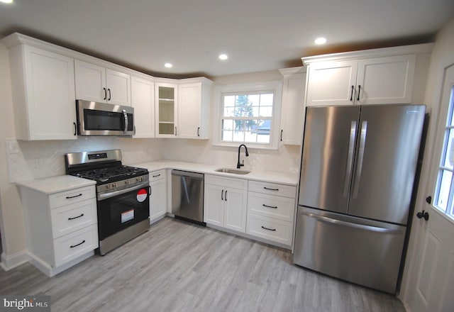 kitchen featuring backsplash, white cabinets, sink, light hardwood / wood-style floors, and stainless steel appliances