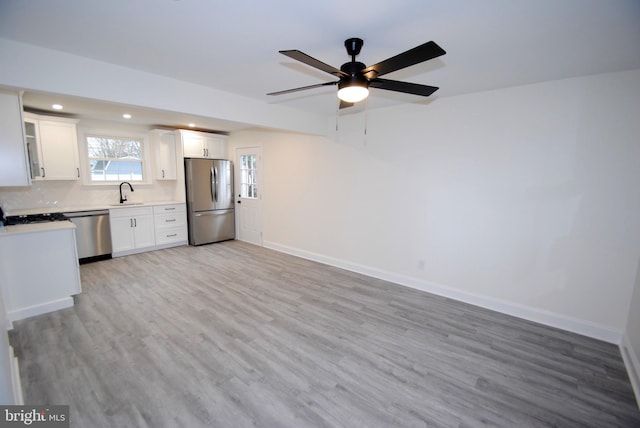 kitchen with stainless steel appliances, ceiling fan, sink, white cabinets, and light hardwood / wood-style floors