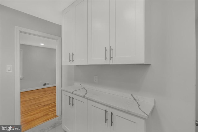 interior space with white cabinetry, light stone counters, and light wood-type flooring