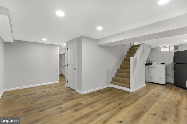 basement with black fridge, washer and clothes dryer, and light wood-type flooring