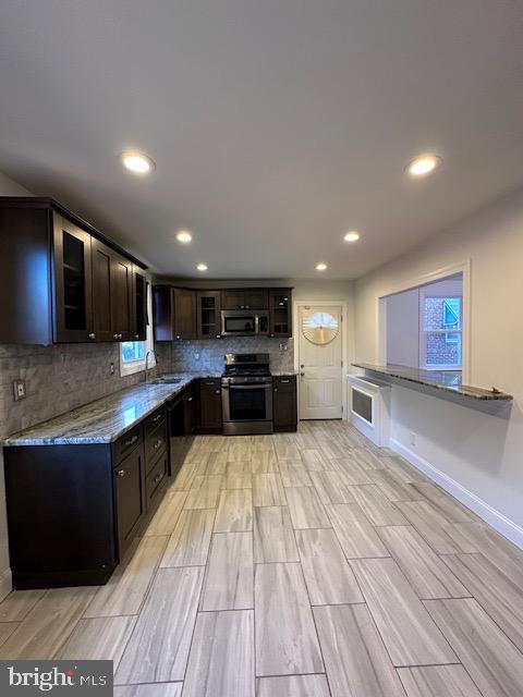 kitchen with light stone countertops, decorative backsplash, dark brown cabinets, stainless steel appliances, and sink