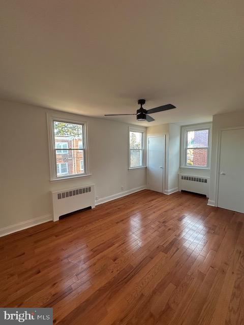 unfurnished room featuring radiator, hardwood / wood-style floors, and a healthy amount of sunlight