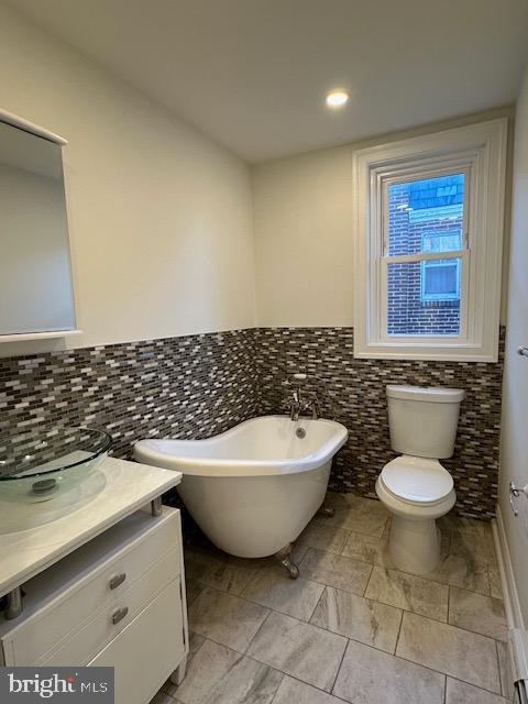 bathroom featuring vanity, a tub to relax in, and toilet