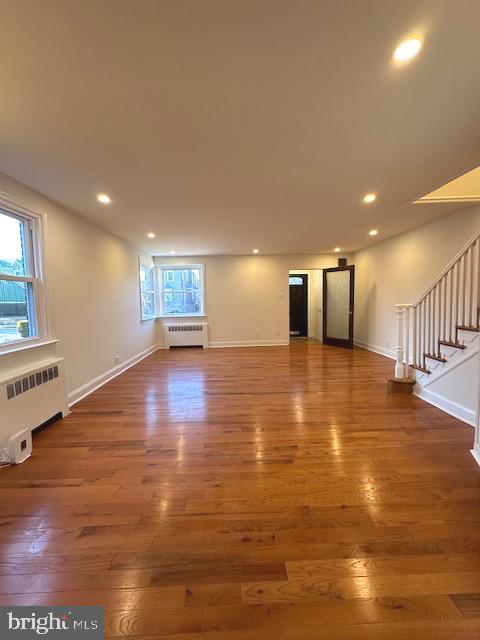 unfurnished living room with hardwood / wood-style floors, plenty of natural light, and radiator heating unit