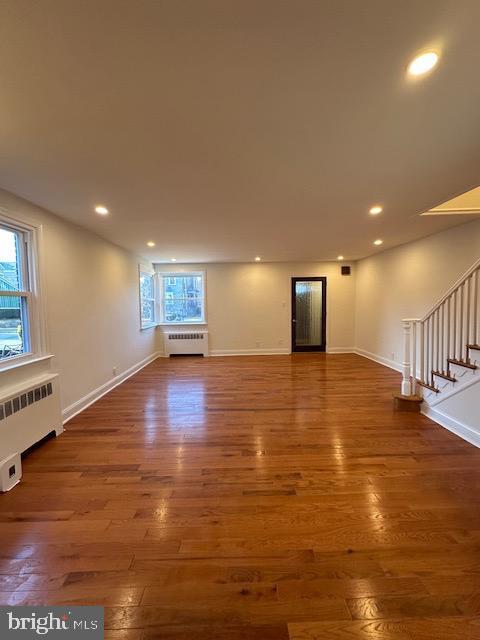 unfurnished living room featuring radiator, dark hardwood / wood-style floors, and plenty of natural light