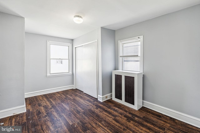 unfurnished bedroom with a closet, dark hardwood / wood-style flooring, and multiple windows