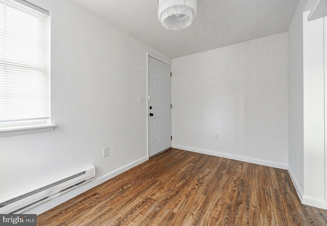 spare room featuring a healthy amount of sunlight, dark hardwood / wood-style floors, and a baseboard heating unit