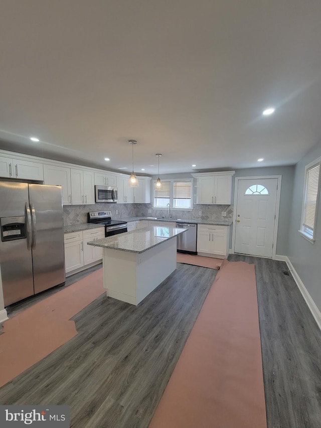 kitchen with stainless steel appliances, decorative light fixtures, white cabinets, a center island, and dark hardwood / wood-style floors