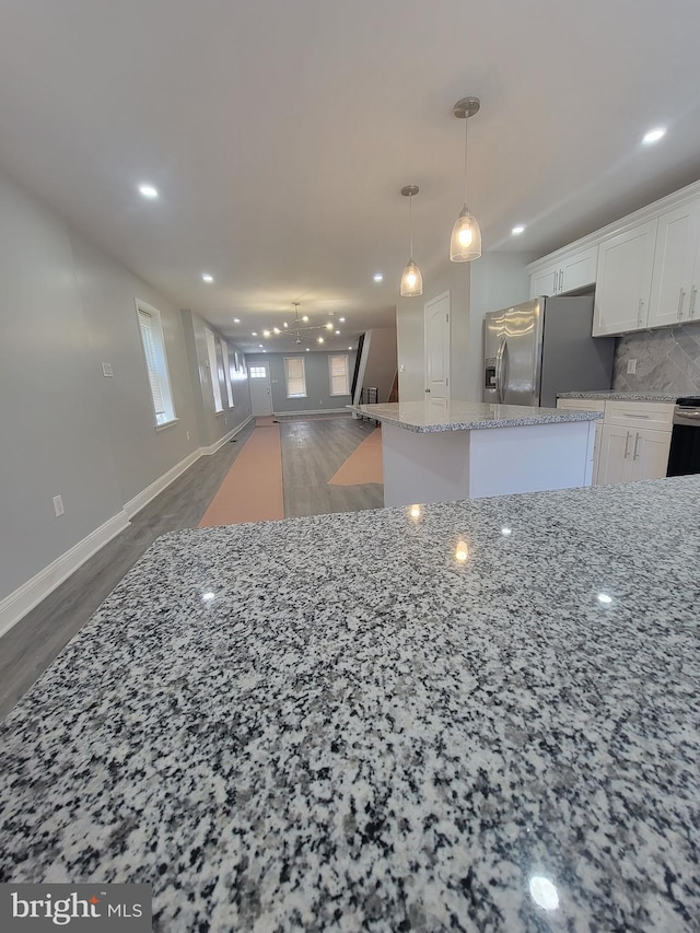 kitchen with light stone countertops, stainless steel refrigerator with ice dispenser, dark hardwood / wood-style flooring, tasteful backsplash, and white cabinets