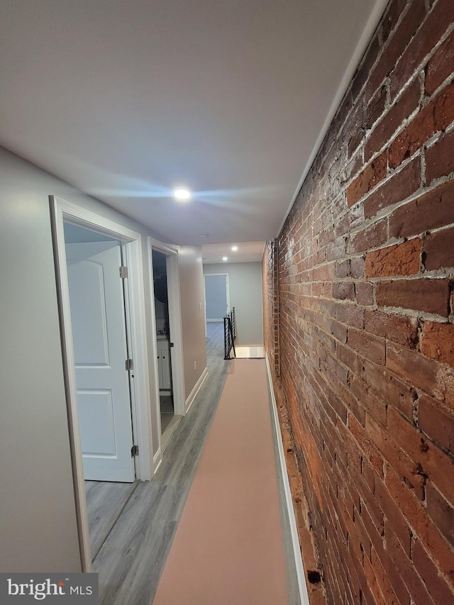 hallway featuring light wood-type flooring and brick wall