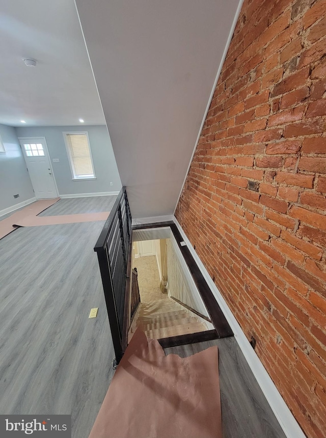 stairs featuring wood-type flooring and brick wall